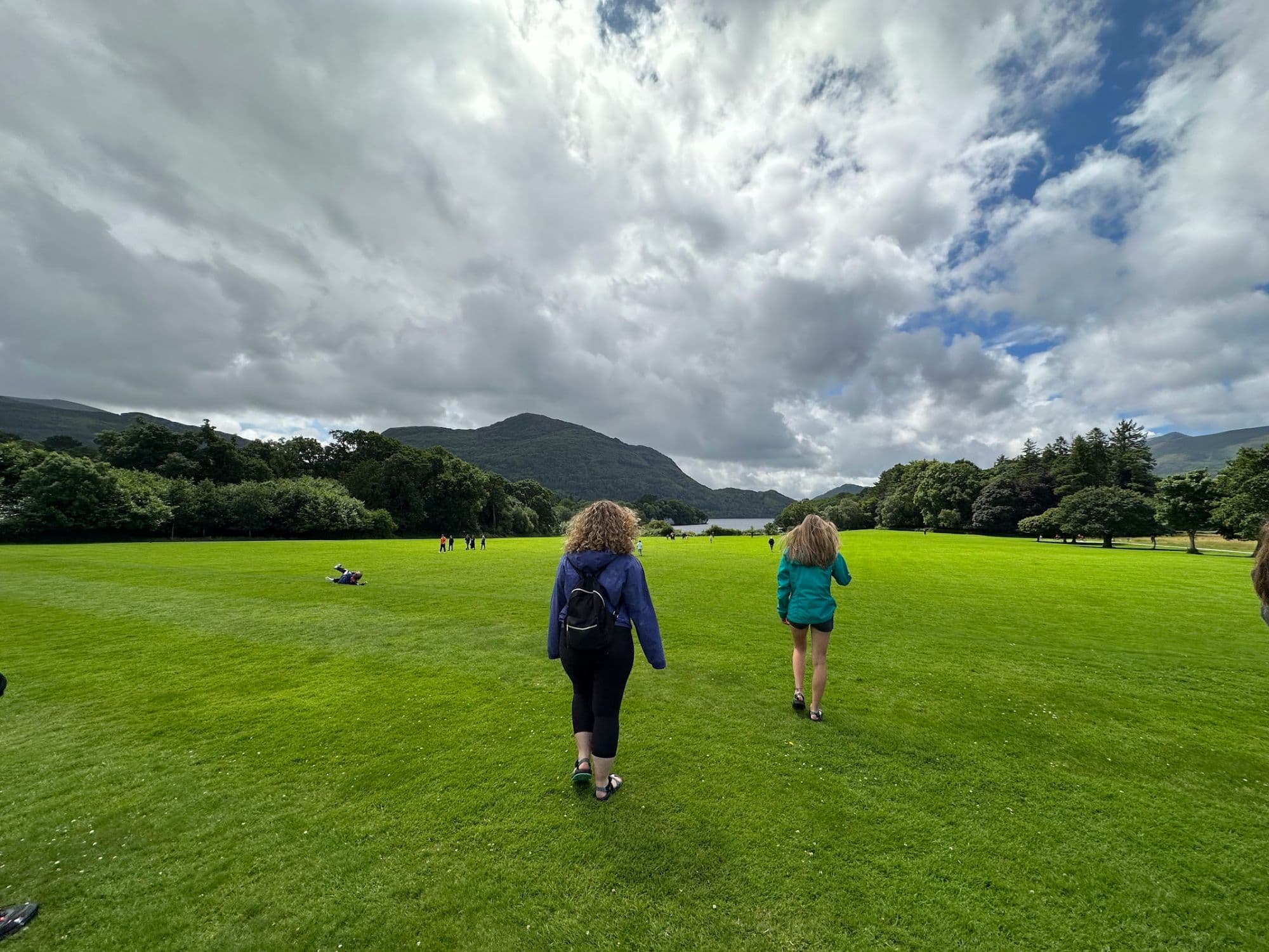 Two Irish Way students walking across a lawn toward a lake and mountains in Ireland